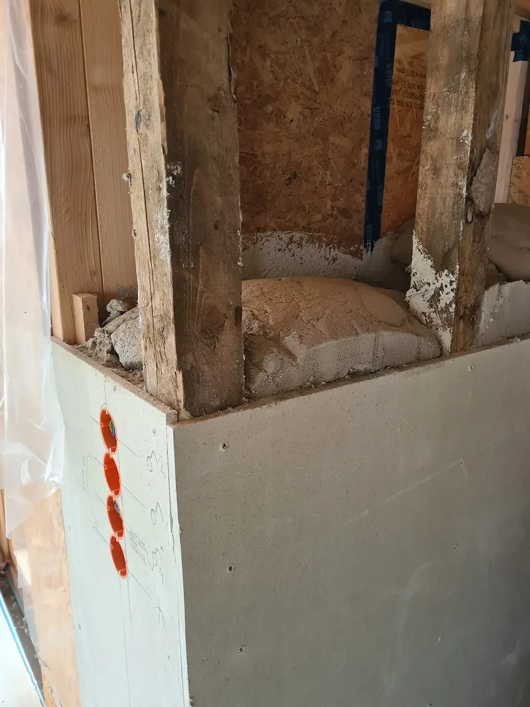 Eckbereich einer Wandkonstruktion mit Holzstützen, teils eingebautem Dämmmaterial und vorbereiteten Elektrodosen